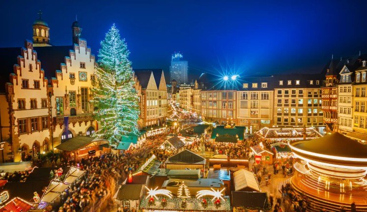 European Christmas market at night with illuminated tree and historic buildings
