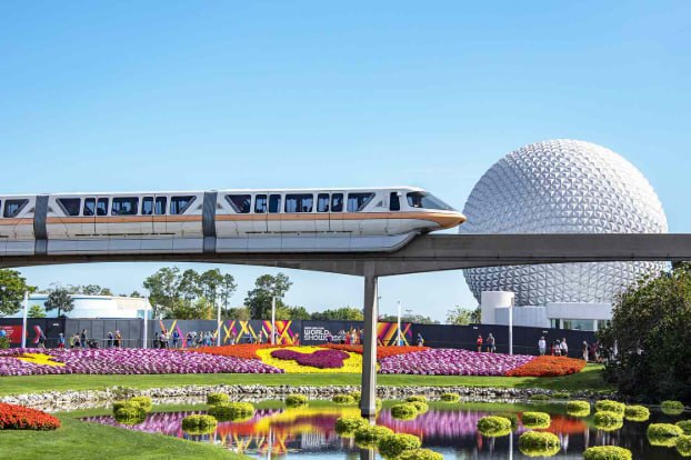 An EPCOT monorail glides past Spaceship Earth and the Flower & Garden Festival displays